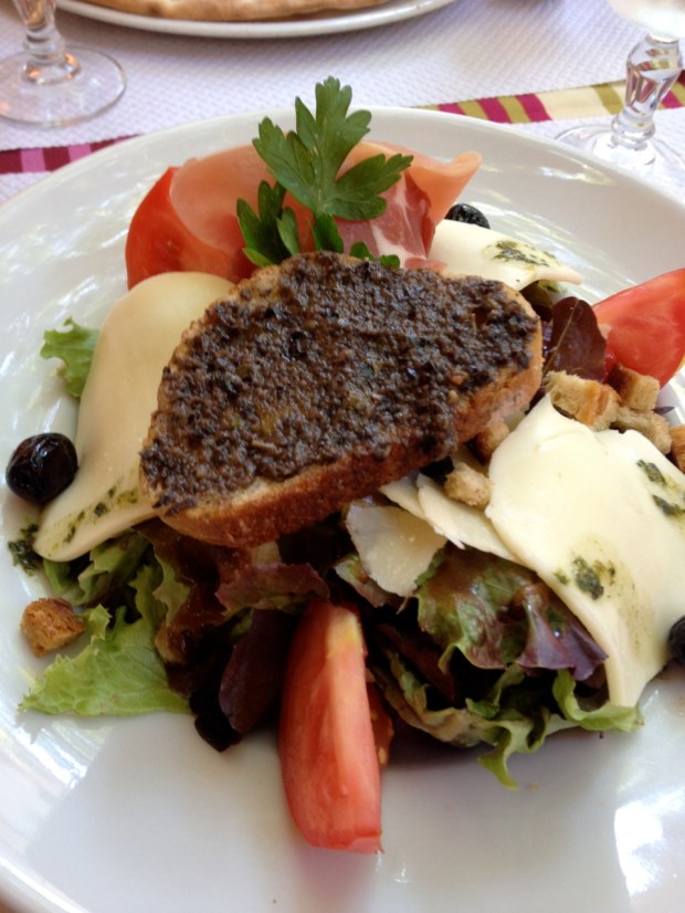 Salad. On the bread is an olive tapenade and behind it is a big strip of prosciutto.